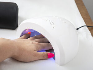 Female hand with pink nails in the lamp for manicure